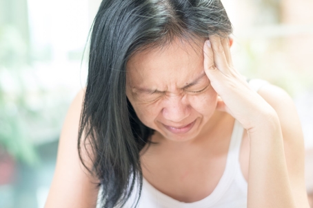 woman with eyes closed holding head in pain