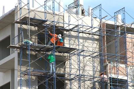 construction workers on scaffolding wearing brightly colored vests and hard hats